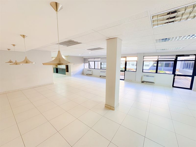 Spacious, open-plan office area featuring ceramic tile flooring, suspended ceilings with recessed lighting, and large windows providing ample natural light.