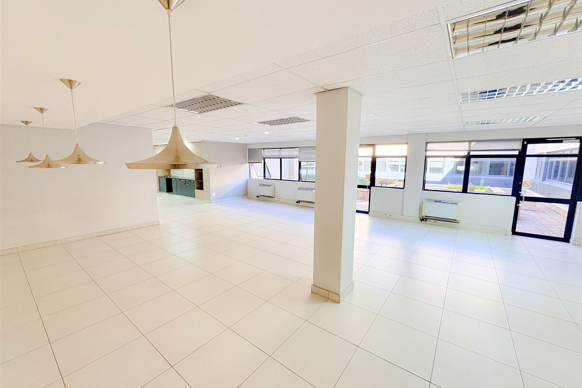 Spacious, open-plan office area featuring ceramic tile flooring, suspended ceilings with recessed lighting, and large windows providing ample natural light.
