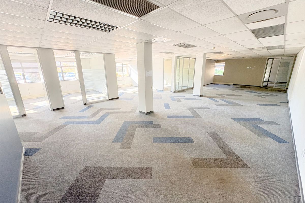 Spacious open-plan office area featuring suspended ceilings, recessed lighting, glass partitioning, and patterned carpet tiles throughout.