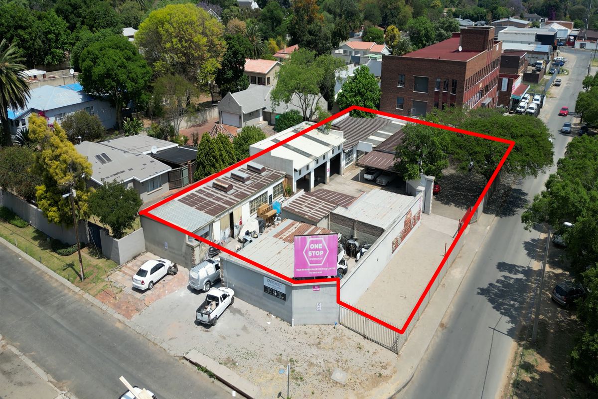 Aerial view of an industrial workshop property featuring multiple bays, secure perimeter fencing, and corner street access in a mixed-use area.