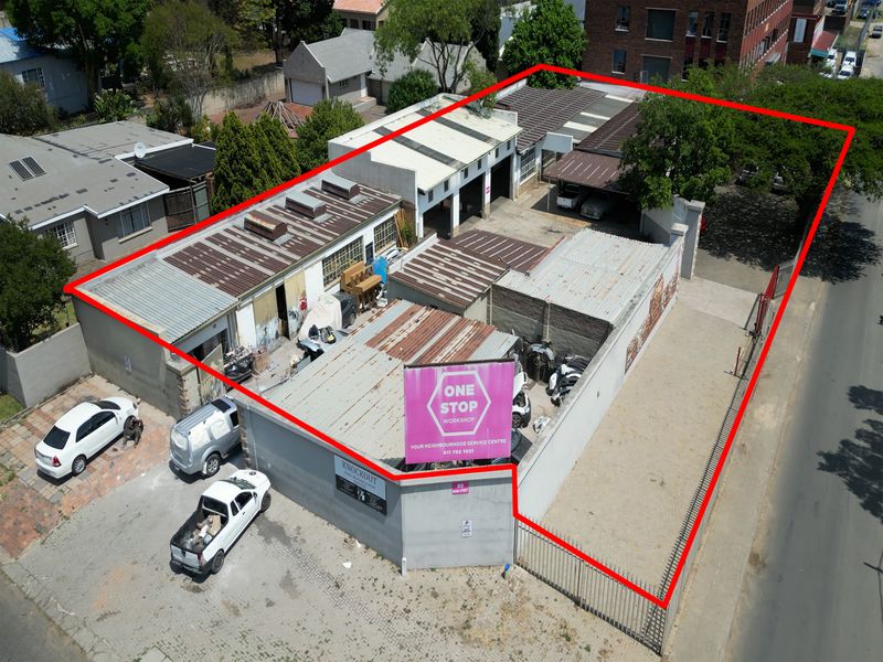Aerial view of an industrial workshop property featuring multiple bays, corrugated metal roofing, and a secure perimeter fence with street access.