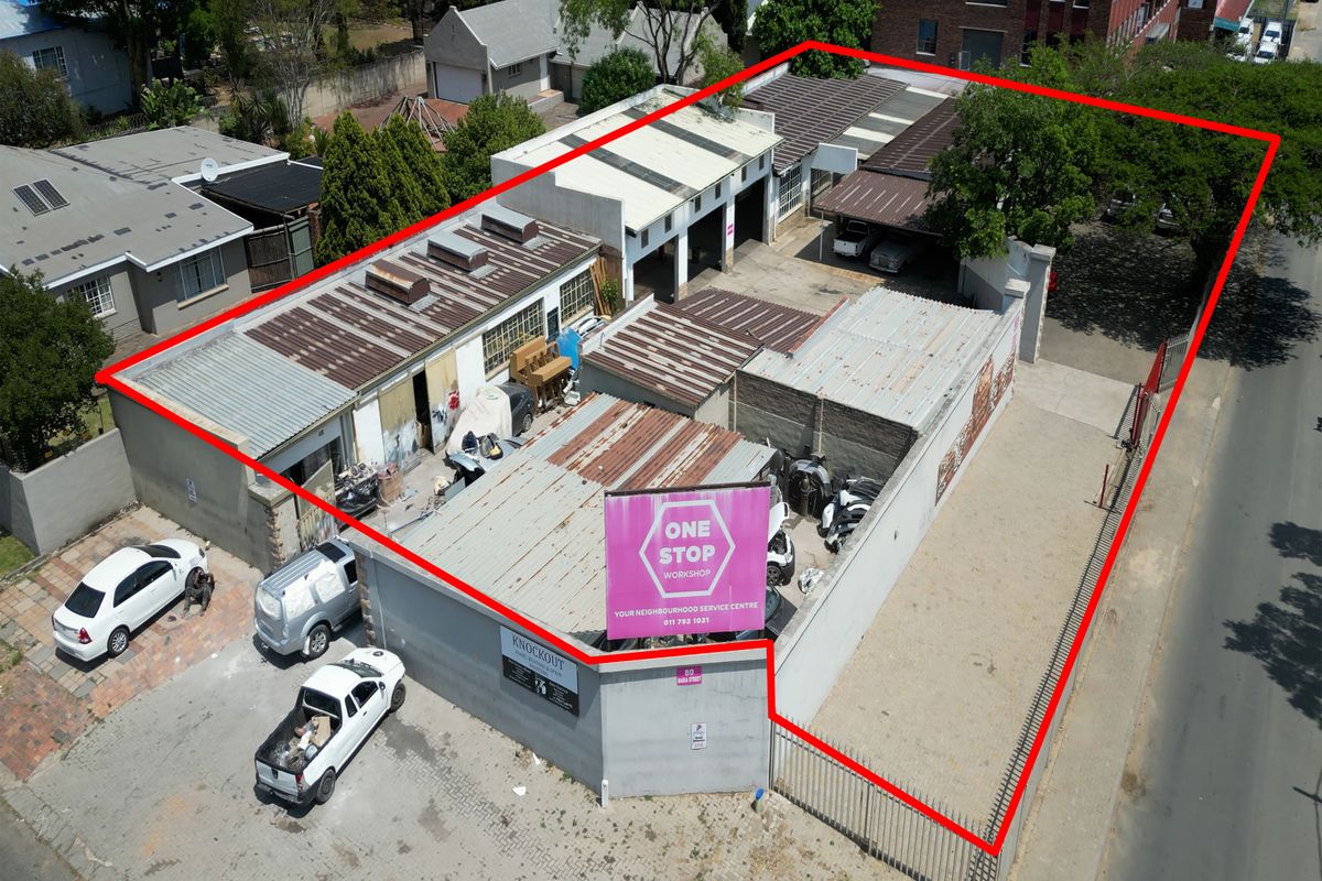 Aerial view of an industrial workshop property featuring multiple bays, corrugated metal roofing, and a secure perimeter fence with street access.