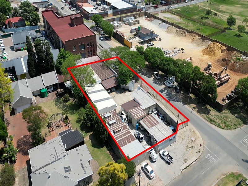 Aerial view of an industrial property featuring multiple warehouse structures, corrugated metal roofing, and a fenced yard area in an urban setting.