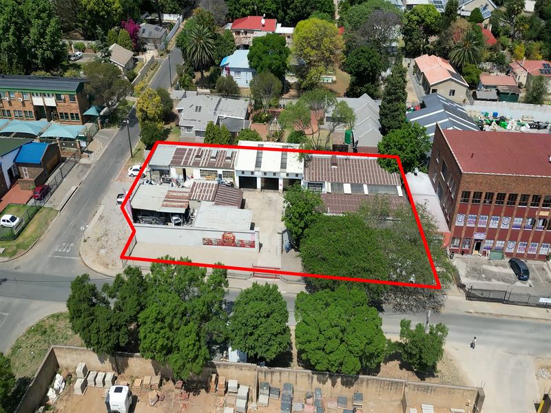Aerial view of an industrial property featuring multiple workshop bays, corrugated metal roofing, and a paved yard area within a fenced perimeter.
