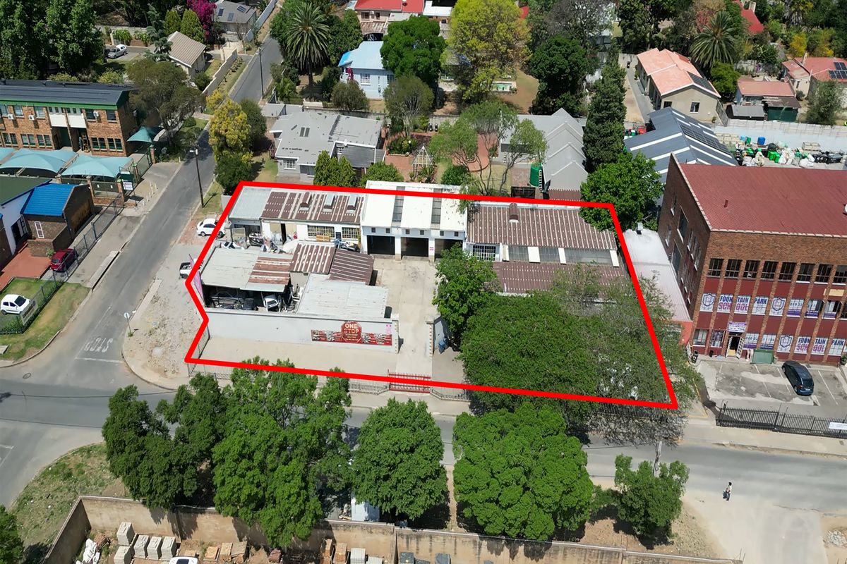 Aerial view of an industrial property featuring multiple workshop bays, corrugated metal roofing, and a paved yard area within a fenced perimeter.