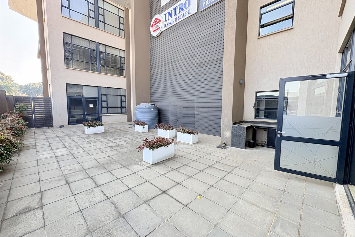 A paved exterior courtyard area featuring aluminium window frames, a water storage tank, and an external service counter attached to the office building facade.