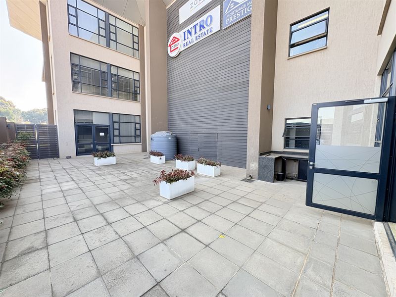 A paved exterior courtyard area featuring aluminium window frames, a water storage tank, and an external service counter attached to the office building facade.