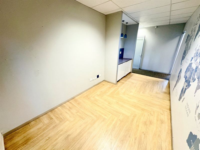 Empty office space featuring herringbone vinyl flooring, a suspended ceiling, and a compact built-in kitchenette area.
