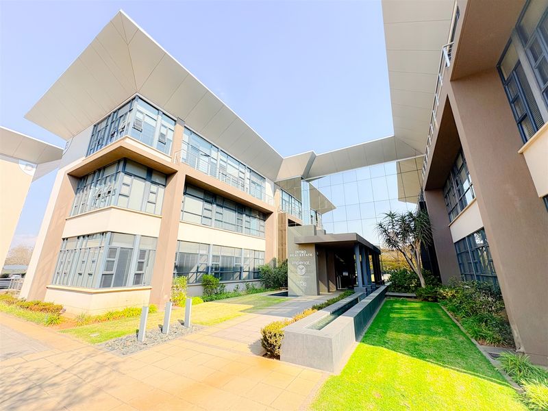 Modern multi-story office building featuring a glass facade, covered entrance, and well-maintained landscaped grounds with a water feature.