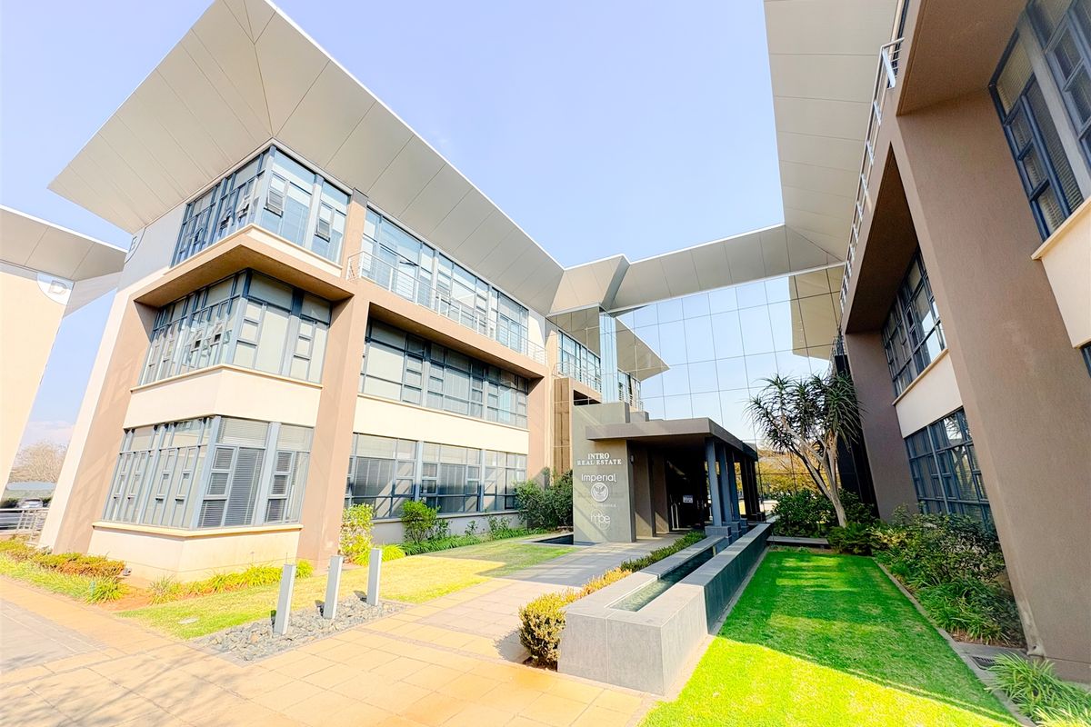 Modern multi-story office building featuring a glass facade, covered entrance, and well-maintained landscaped grounds with a water feature.