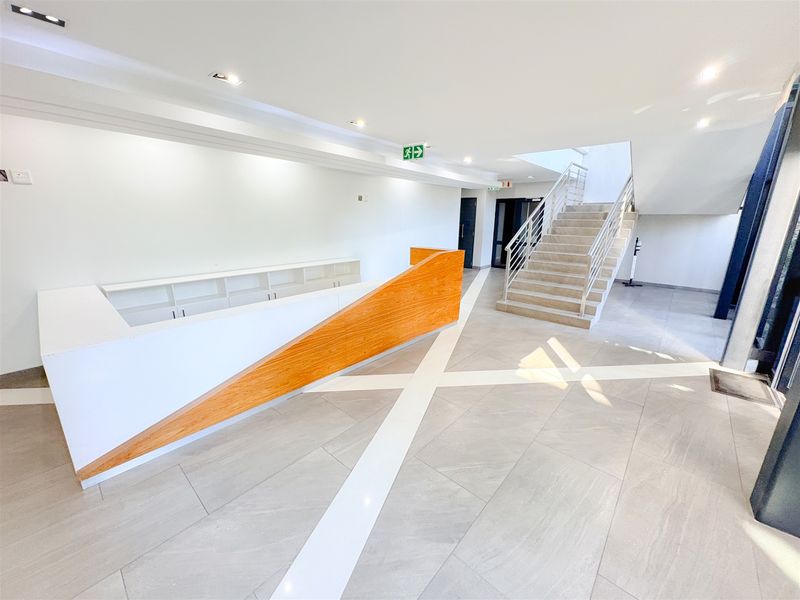 Modern office entrance lobby featuring a sleek built-in reception desk, tiled flooring, and a central staircase leading to upper levels.