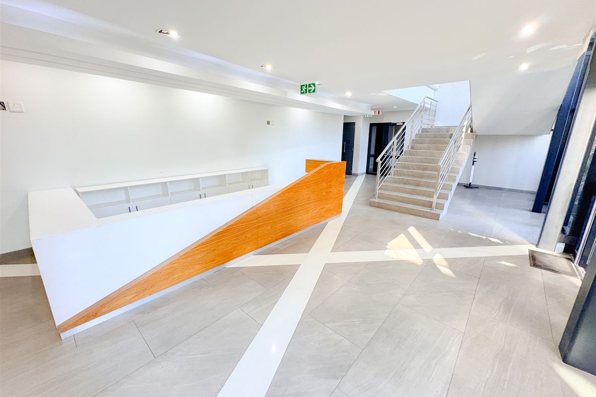 Modern office entrance lobby featuring a sleek built-in reception desk, tiled flooring, and a central staircase leading to upper levels.