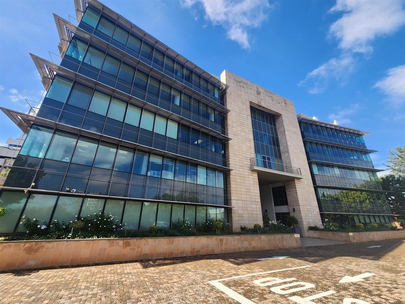 Modern multi-story office building featuring a contemporary glass curtain wall facade, stone cladding, and a paved entrance area.