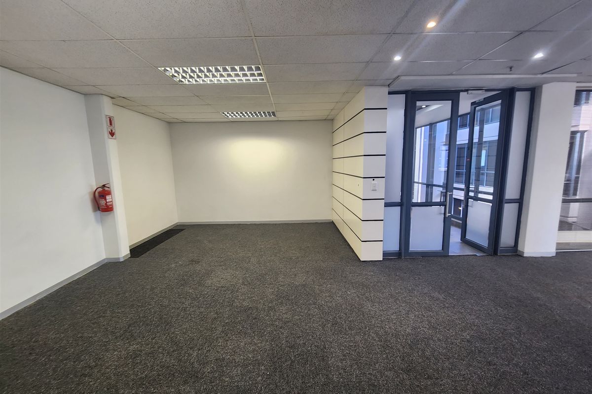 A clean, empty office space featuring a suspended ceiling, recessed lighting, and carpeted flooring with a glass entrance door.