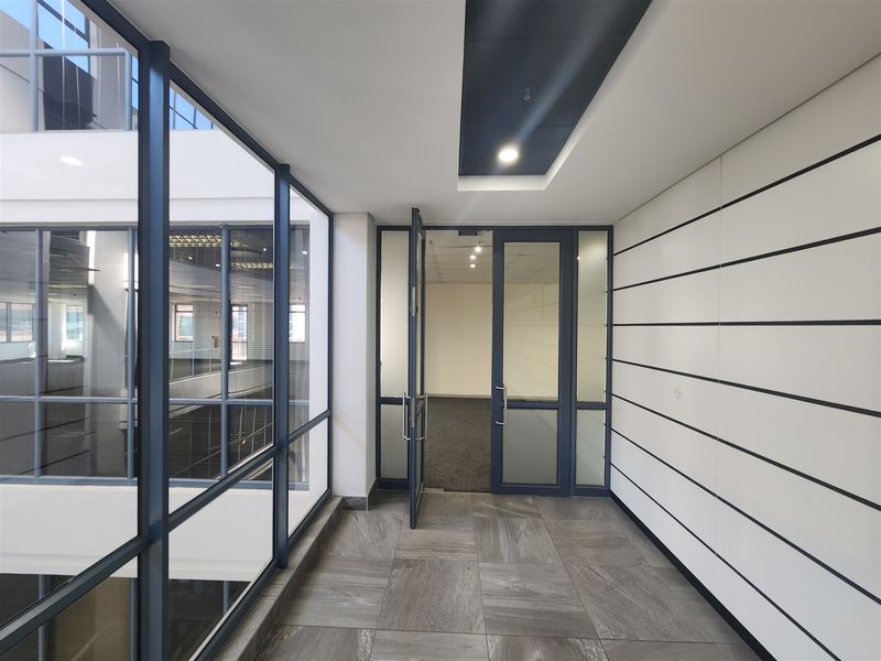 Modern office entrance area featuring glass partitions, sleek tiled flooring, and recessed ceiling lighting, providing a professional and bright workspace environment.
