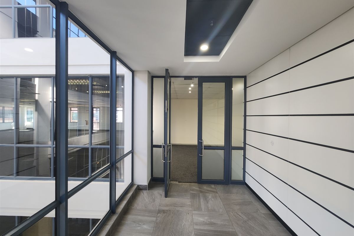 Modern office entrance area featuring glass partitions, sleek tiled flooring, and recessed ceiling lighting, providing a professional and bright workspace environment.