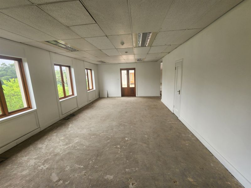 An empty office space featuring a suspended ceiling, recessed lighting, and timber-framed windows, requiring flooring and ceiling repairs.