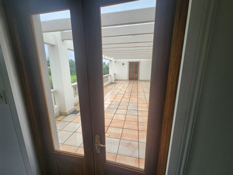 Spacious outdoor balcony featuring a pergola, tiled flooring, and a balustrade, accessible through double glass doors.