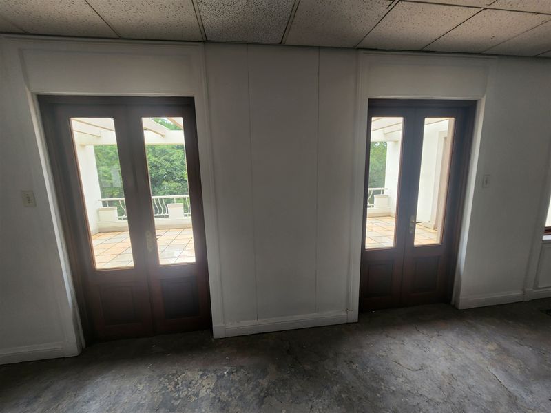 Empty office space featuring dual glass doors leading to an outdoor balcony, with a suspended ceiling and worn flooring throughout.