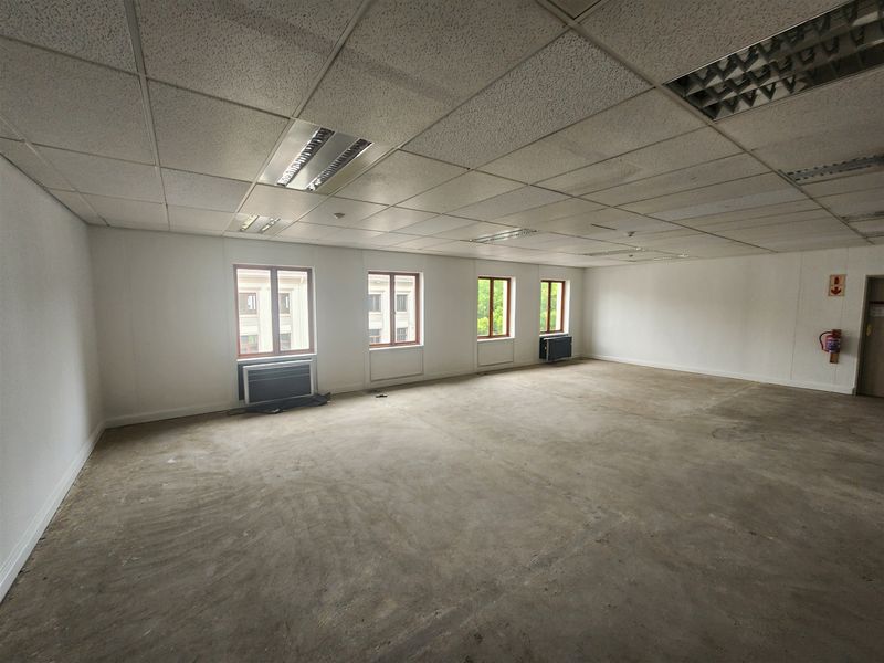 A spacious, vacant office area featuring a suspended ceiling, recessed lighting, air conditioning units, and unfinished concrete flooring, ready for custom fit-out.