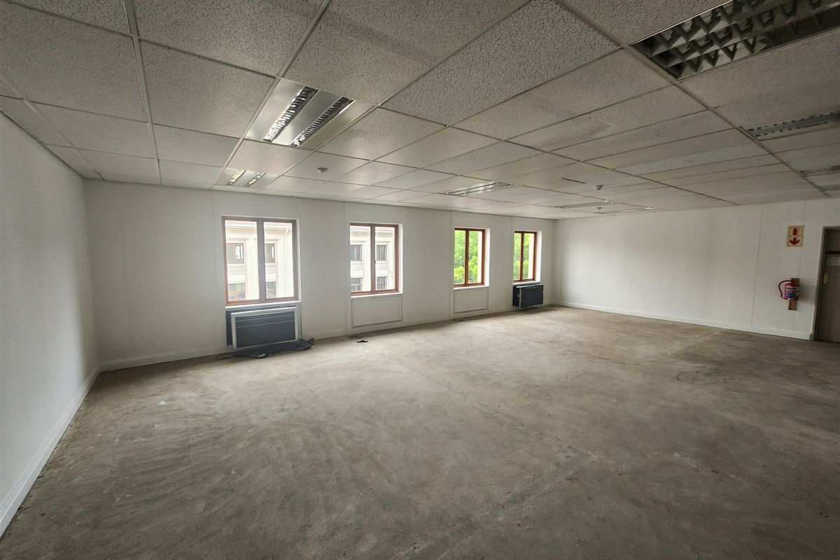 A spacious, vacant office area featuring a suspended ceiling, recessed lighting, air conditioning units, and unfinished concrete flooring, ready for custom fit-out.