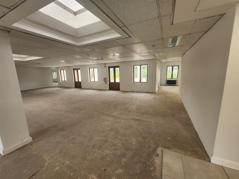 A large, open-plan office space featuring a suspended ceiling with integrated skylights, multiple windows, and exposed concrete flooring ready for refurbishment.