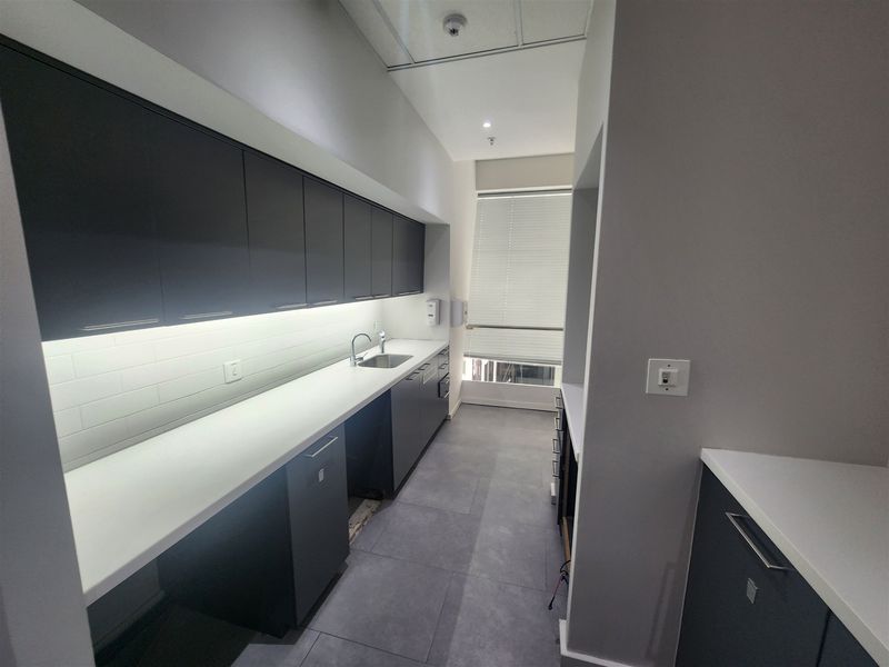 Modern office kitchenette featuring dark cabinetry, white countertops, subway tile backsplash, and tiled flooring, providing a clean and functional break area.