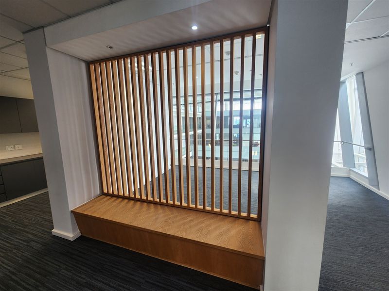 Modern office space featuring a decorative timber slat room divider and integrated built-in bench seating with neutral carpet flooring.