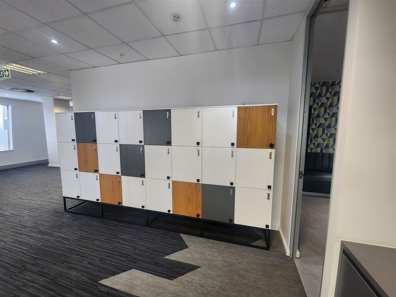 Modern office space featuring a large bank of built-in storage lockers, carpeted flooring, and a suspended ceiling with recessed lighting.