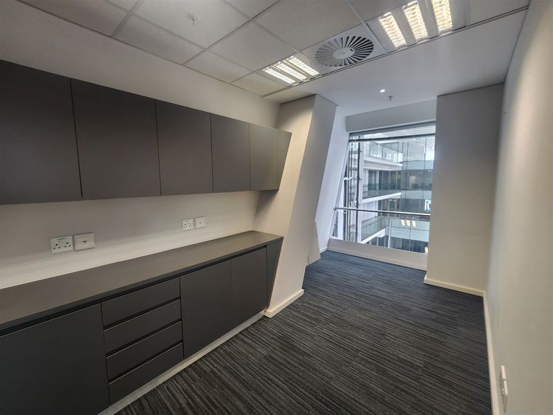 Modern office space featuring built-in dark grey cabinetry, carpeted flooring, recessed lighting, and a large window overlooking the building atrium.