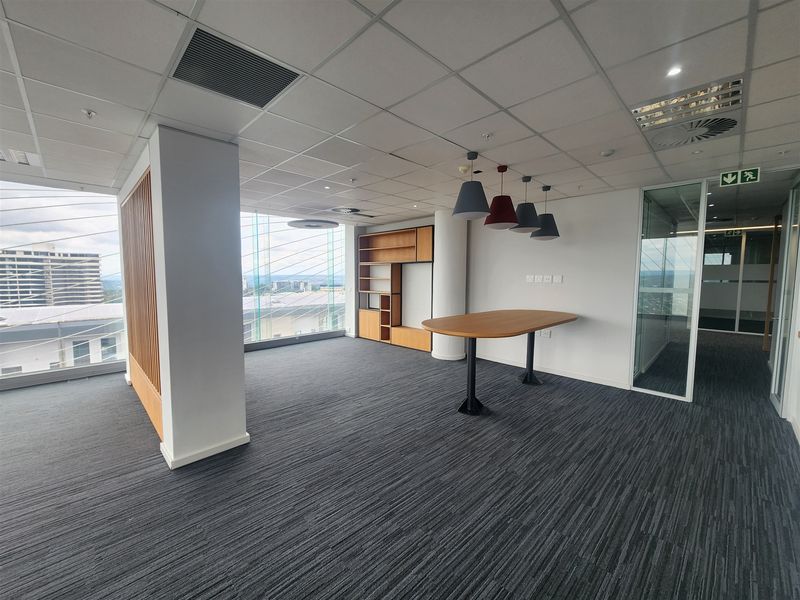 Modern office space featuring floor-to-ceiling windows, carpeted flooring, a suspended ceiling, and a built-in shelving unit with glass partition access.