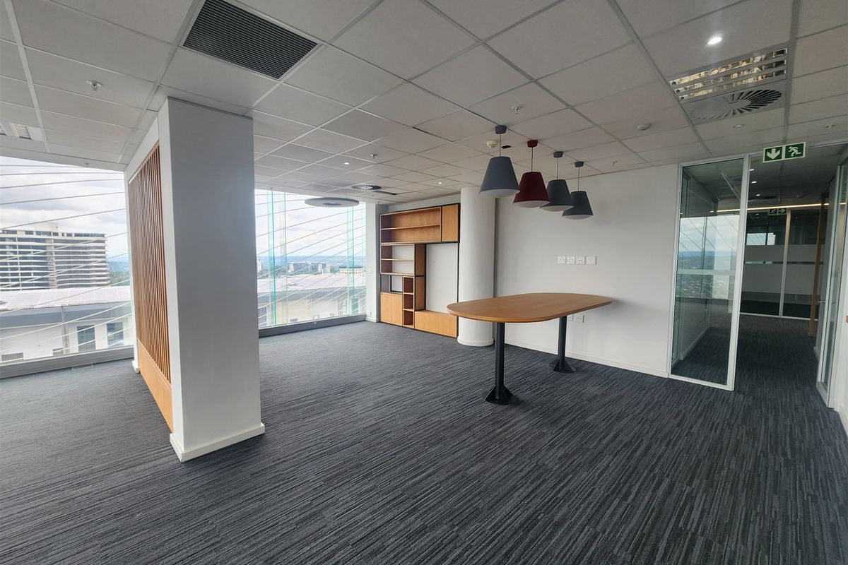 Modern office space featuring floor-to-ceiling windows, carpeted flooring, a suspended ceiling, and a built-in shelving unit with glass partition access.