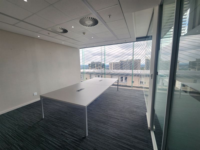 Modern office space featuring floor-to-ceiling glass windows with city views, suspended ceilings, recessed lighting, and glass partition walls.