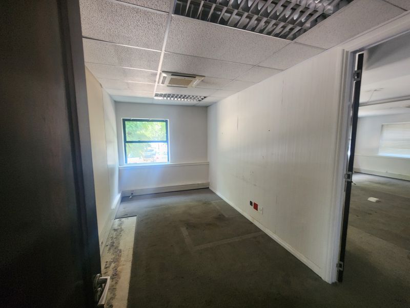 An empty office space featuring a suspended ceiling, recessed lighting, and carpet flooring, requiring cosmetic updates to the walls and floor finishes.