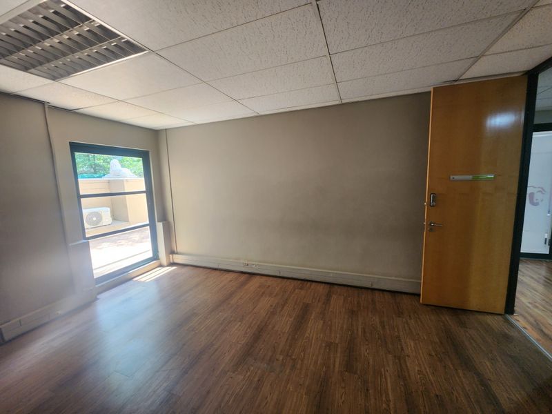 A vacant office space featuring laminate flooring, a suspended ceiling with recessed lighting, and a large window providing natural light.