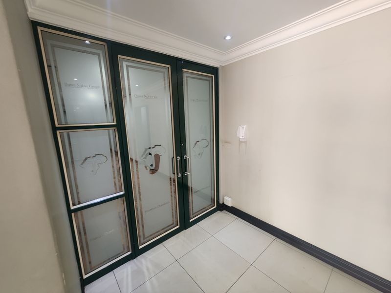A clean and professional office entrance featuring modern tiled flooring, recessed lighting, and branded frosted glass double doors.