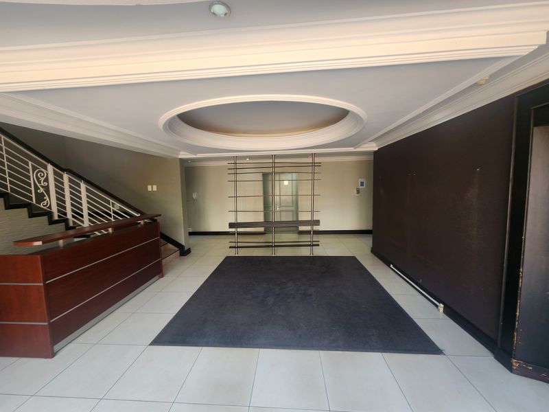 Spacious office building entrance lobby featuring a reception desk, staircase with metal balustrade, and decorative recessed ceiling detail.