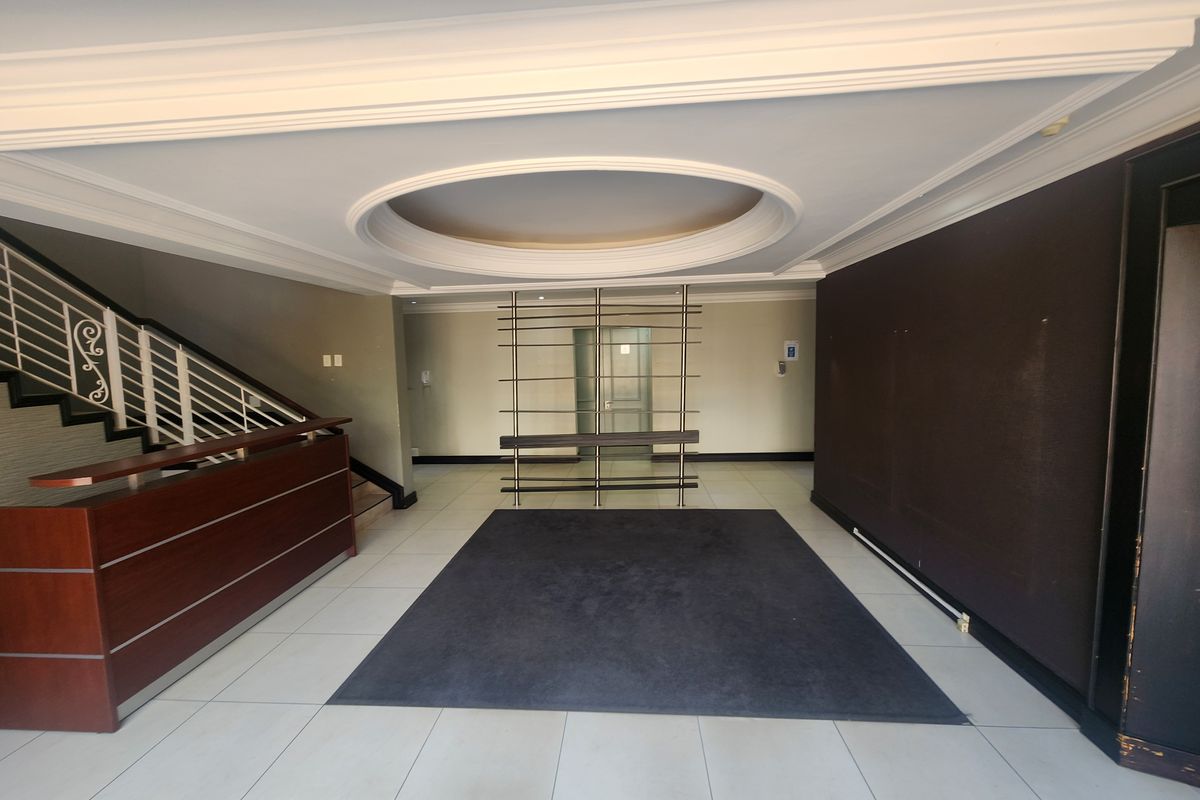 Spacious office building entrance lobby featuring a reception desk, staircase with metal balustrade, and decorative recessed ceiling detail.
