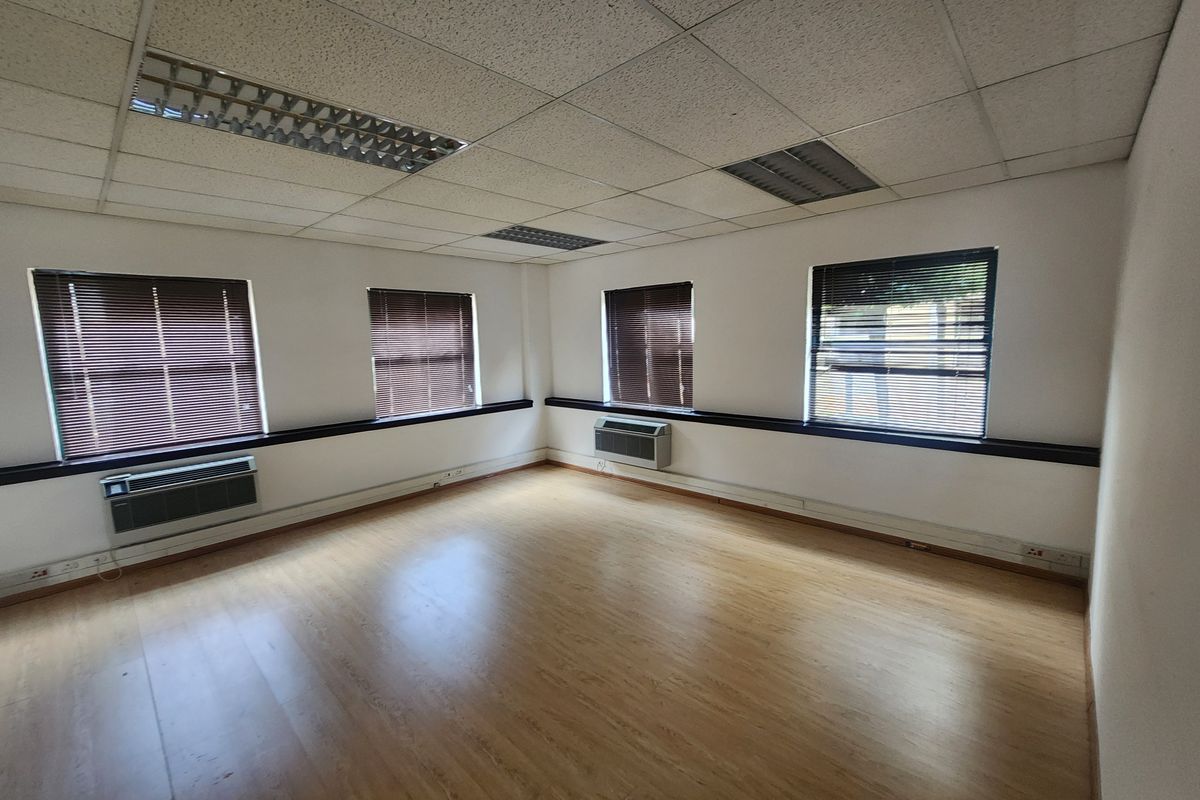 A bright, empty office space featuring laminate flooring, suspended ceilings with recessed lighting, and wall-mounted air conditioning units.
