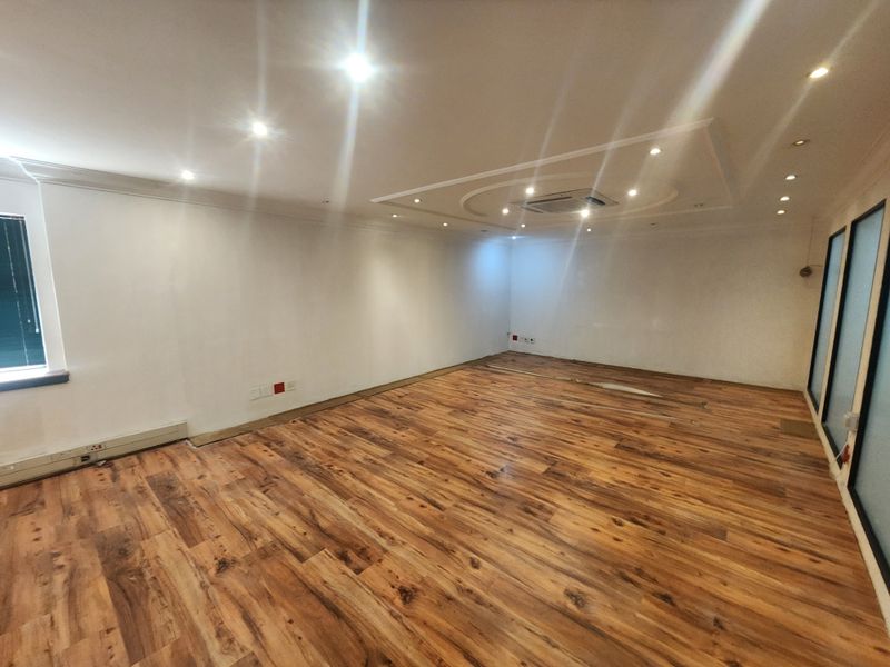 A spacious, empty office area featuring modern laminate wood flooring, a decorative coffered ceiling with recessed lighting, and integrated ducted air conditioning.