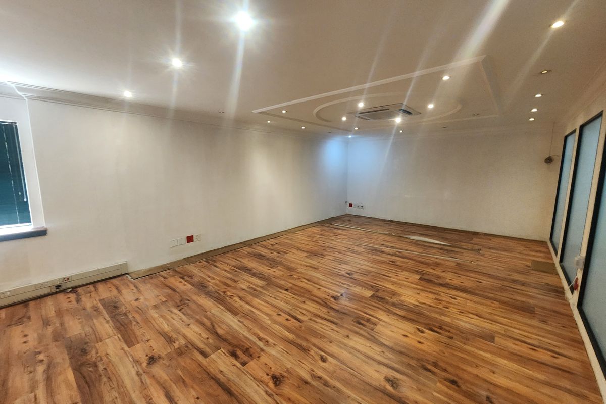 A spacious, empty office area featuring modern laminate wood flooring, a decorative coffered ceiling with recessed lighting, and integrated ducted air conditioning.