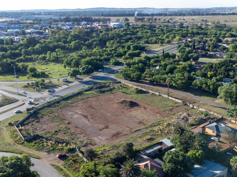 Aerial view of a vacant, undeveloped commercial plot situated near a road intersection, surrounded by established residential and industrial areas.