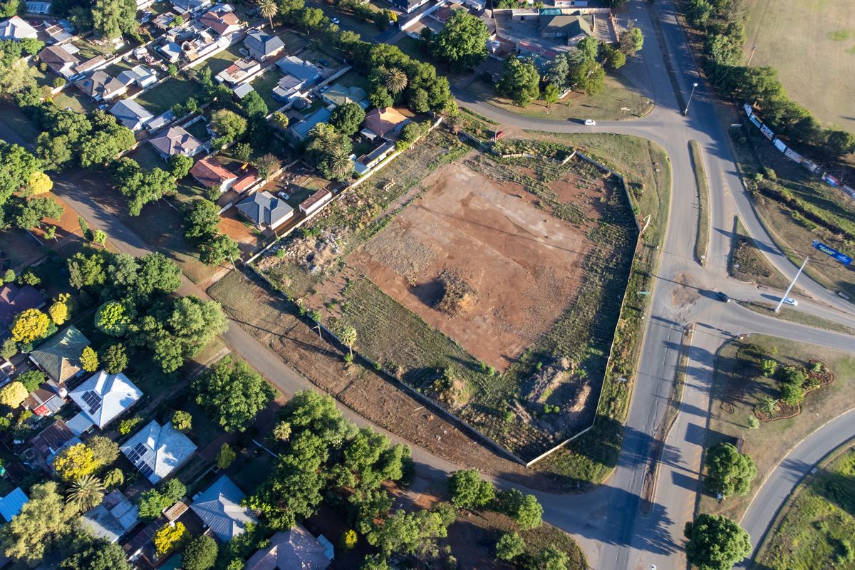 Aerial view of a vacant, undeveloped corner plot situated in a residential area, offering significant potential for future retail or commercial development.