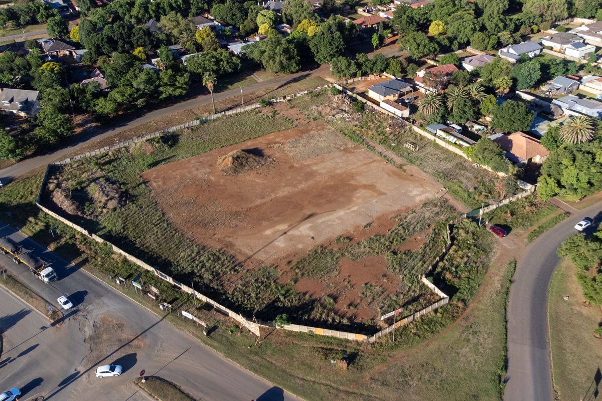 An aerial view of a vacant corner plot of land, featuring perimeter fencing and direct access from two adjacent suburban roads.