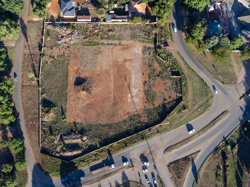 Aerial view of a vacant corner plot of land, showing cleared ground and surrounding residential infrastructure.