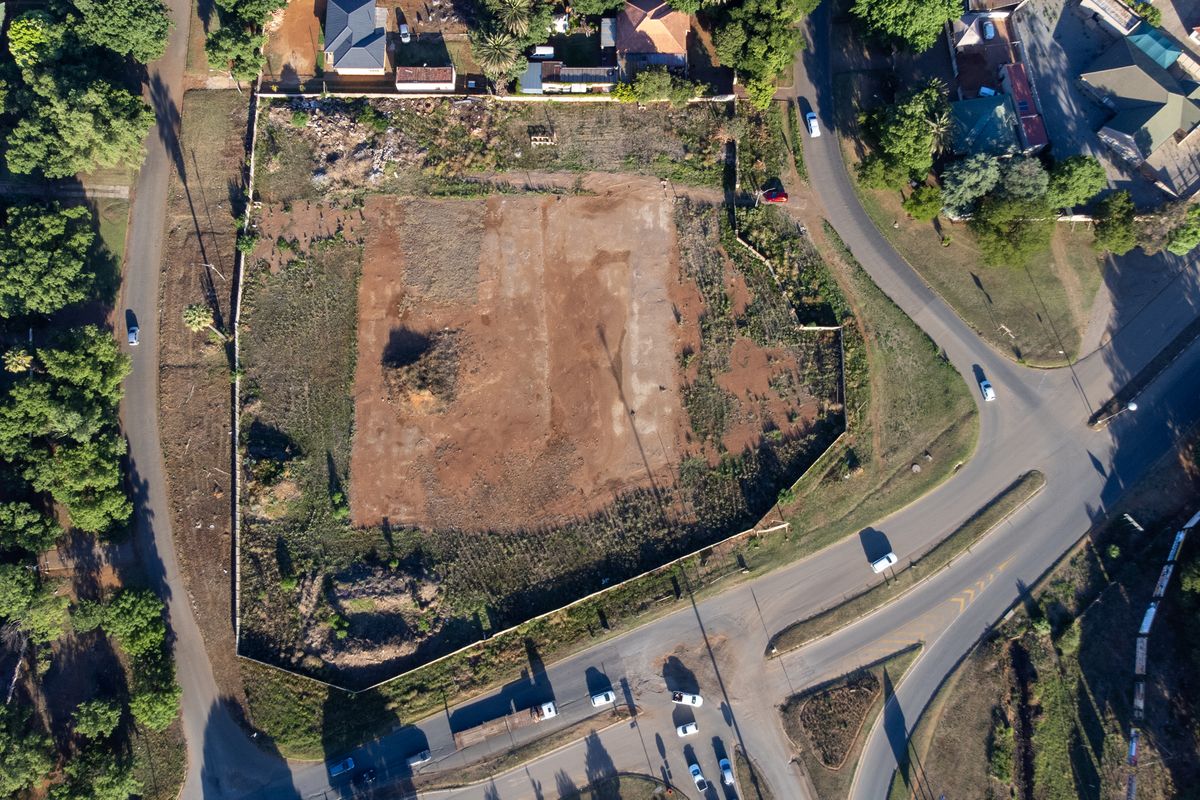 Aerial view of a vacant corner plot of land, showing cleared ground and surrounding residential infrastructure.