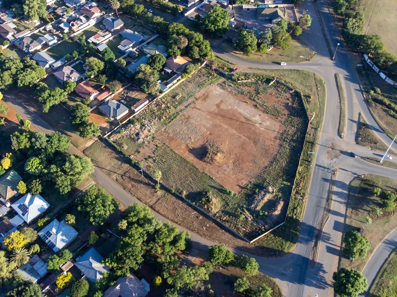 Aerial view of a vacant, undeveloped corner plot situated in a residential area, offering significant potential for future retail or commercial development.