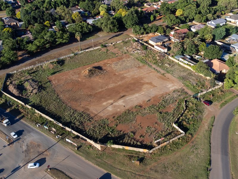 An aerial view of a vacant corner plot of land, featuring perimeter fencing and direct access from two adjacent suburban roads.