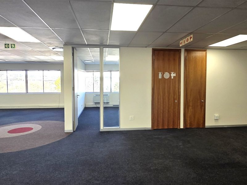 Spacious open-plan office area featuring suspended ceilings, recessed lighting, carpeted floors, and a separate partitioned office space with large windows.