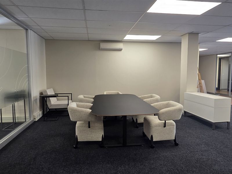 A modern office space featuring a glass partition, suspended ceiling with recessed lighting, split-system air conditioning, and dark carpet flooring.